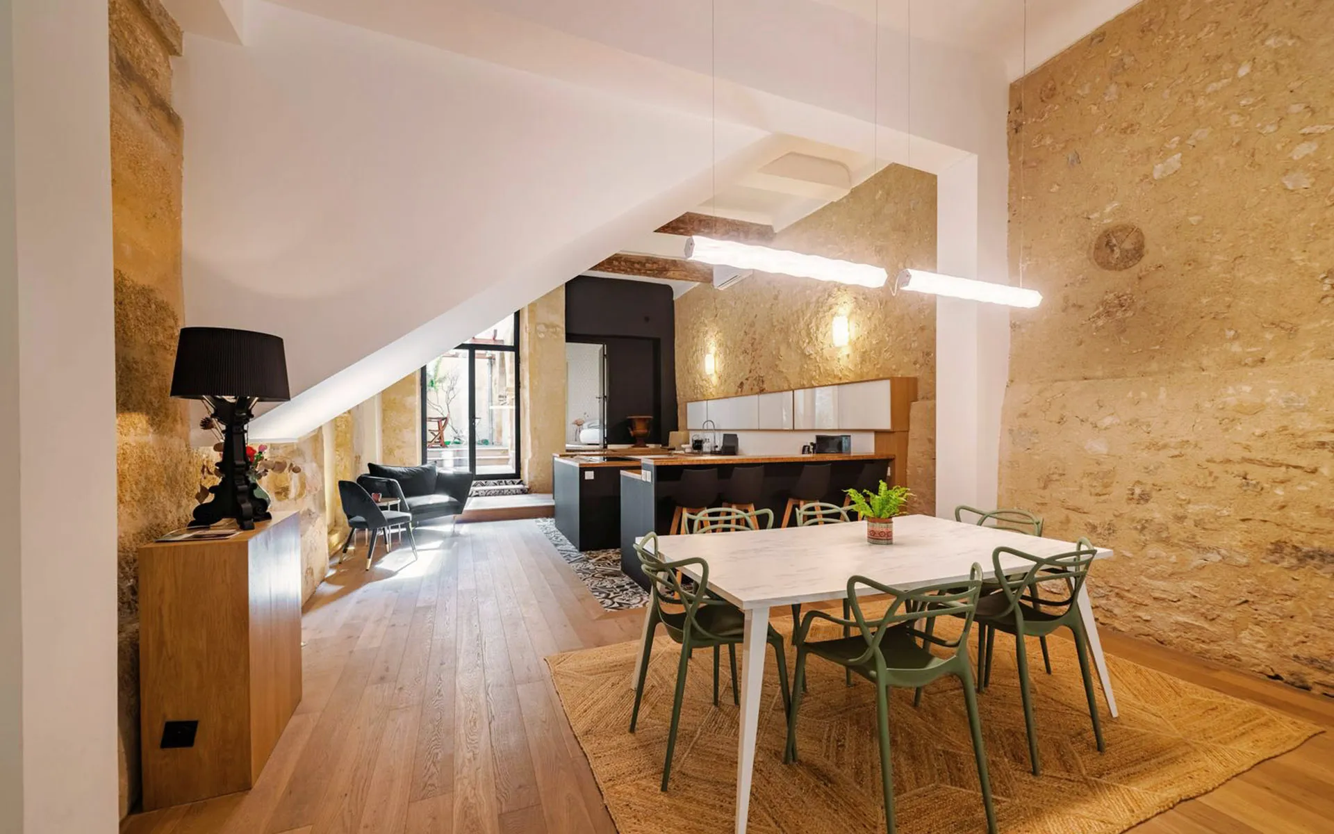 Salle à manger sous pente, poutre et mur de pierre, chaises vertes.